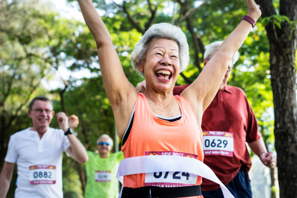 heureux principal qui traverse la ligne d’arrivée - running jogging asian ethnicity women photos et images de collection