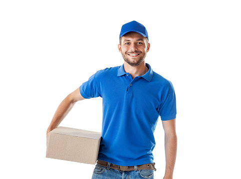 Happy young delivery man in blue uniform standing with parcel post box isolated on white background