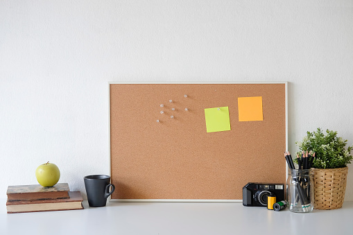 Stylish table Board and post it, book, pencil, camera  and coffee mug on table with wall.