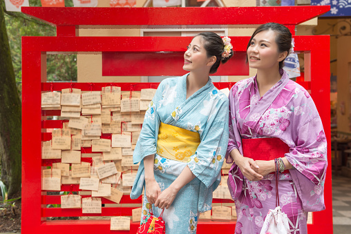Two Asian woman standing side by side in front of the wish wall and looking to the same direction.