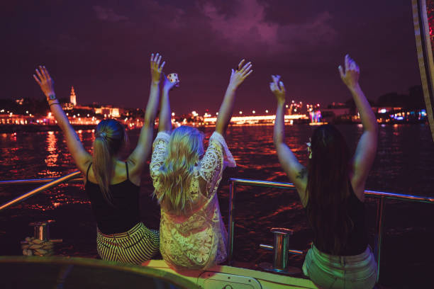 Ladies enjoying on the boat at night Three women are sitting with hands raised on the deck of the boat at night. bachelor and bachelorette parties stock pictures, royalty-free photos & images