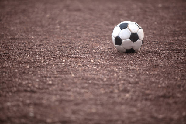 Black and white soccer ball on dirt play ground. No people are seen in frame. Shot in outdoor with a full frame DSLR camera.