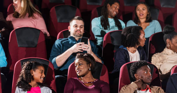 istock Multi-ethnic group in movie theater, man on mobile phone 1023471976