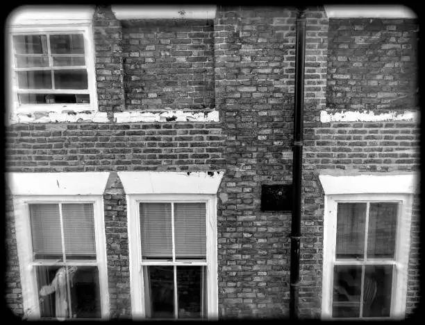 Rear of a row of houses with ghost-like figures in one of the windows.