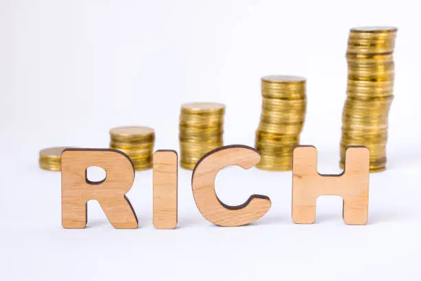Word rich of three-dimensional letters is in foreground with growth columns of coins on blurred background. Rich concept for finance, economics, money, banks, business, startup, investing, markets