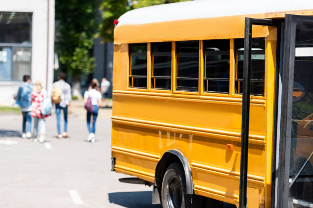 istock traditional school bus standing on parking with blurred students walking on background 1023496352