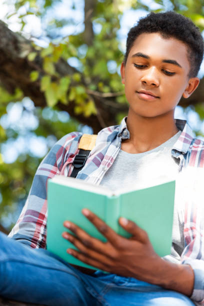 istock bottom view of focused teen student reading book under tree 1023496468