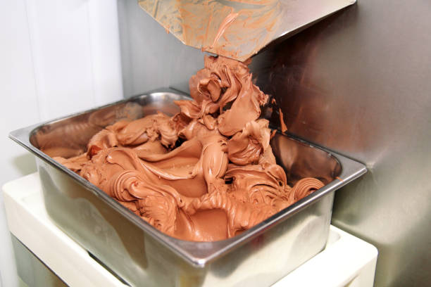 Ice cream making machine produces black chocolate ice cream flavors and it falls into steel container. Industrial preparation of italian creamy ice cream. Producing chocolate ice cream with machine. Ice cream making machine produces black chocolate ice cream flavors and it falls into steel container. Industrial preparation of italian creamy ice cream. Producing chocolate ice cream with machine. stealing ice cream stock pictures, royalty-free photos & images