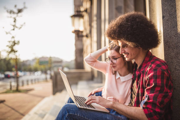 istock A young couple, sitting on a sidewalk wall, browsing the internet on a laptop 1023510130