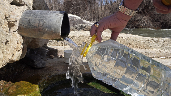 Old man fill plastic bottle with thermal drink water from natural spring