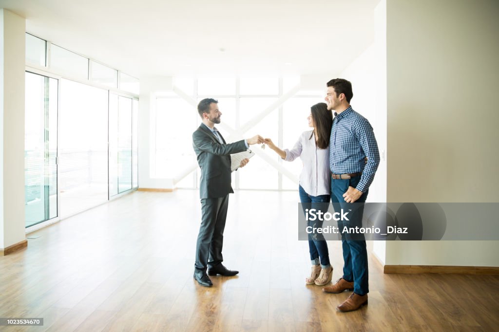 Couple Getting Keys From Real Estate Agent Of Their New Home Happy mid adult couple getting keys from Real Estate Agent of their new home Real Estate Agent Stock Photo
