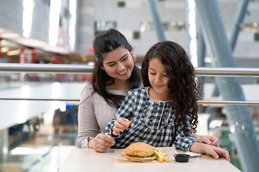 Mother and daughter at the food court in a shopping mall sharing a burger both smiling