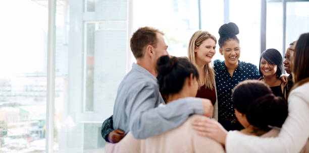 The success of a business leans on it’s team Shot of a group of young businesspeople huddled together in solidarity in a modern office arm around stock pictures, royalty-free photos & images