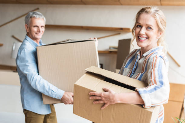 istock happy senior couple holding cardboard boxes and smiling at camera during relocation 1023557506