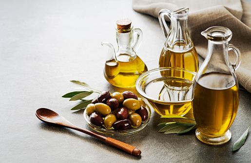 Bottles of Extra virgin healthy Olive oil with fresh olives on gray background