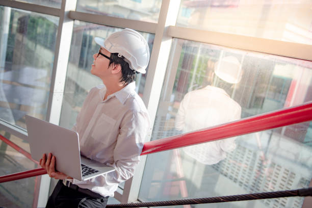 istock Young Asian male engineer or architect working with laptop computer while wearing protective safety helmet at construction site. Architecture, Engineering and building construction concepts 1023560826