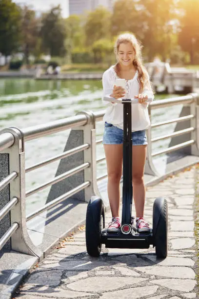 A young beautiful girl with a smartphone is riding a segway in a park. Healthy lifestyle.