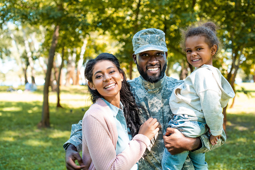 feliz soldado afroamericano en militar uniforme mirando a cámara con la familia en el Parque photo