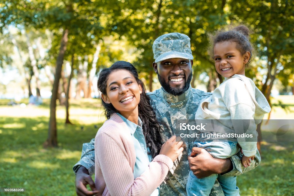 happy african american soldier in military uniform looking at camera with family in park Military Stock Photo
