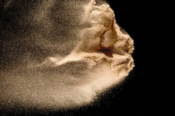 Photo of Dry river sand explosion. Golden colored sand splash against dark background.