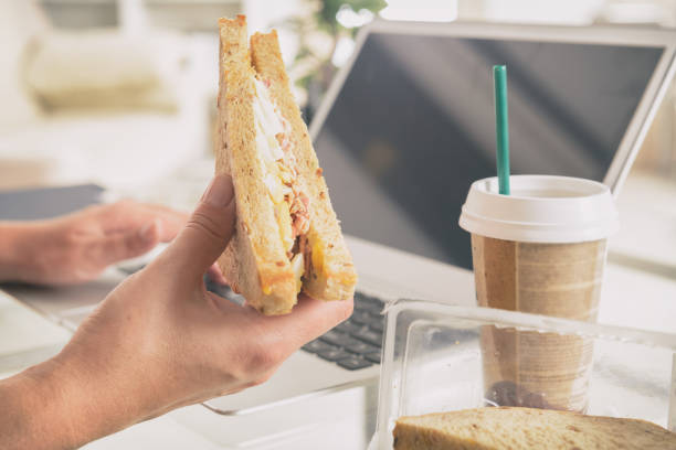 istock Woman eating a breakfast sandwich while working with a laptop 1023608326