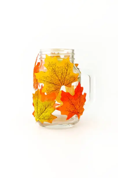 Mason jar decorated with artificial autumn leaves as tealight or candle holder and DIY autumn home decoration.