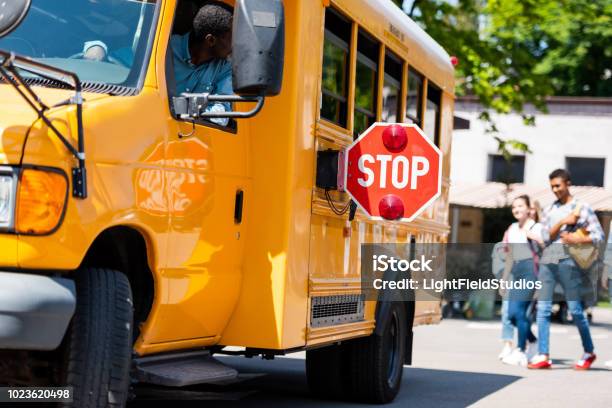 Senior School Bus Driver Looking At Teens Walking Behind Bus Stock Photo - Download Image Now