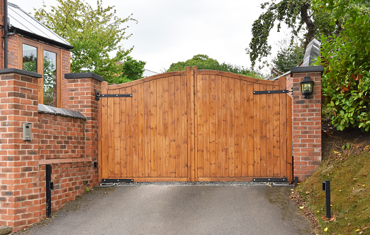 A wooden security gate on the driveway of a residential house with keypad operated lock