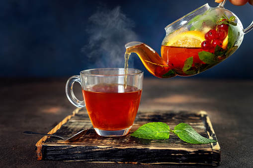 Pouring herbal fruit hot tea in glass cup against dark blue background