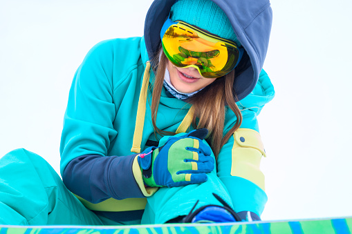 Close up of young snowboarder holding her injured leg.