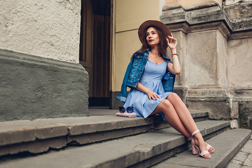Outdoor portrait of young beautiful fashionable woman wearing stylish accessories. Girl sitting on stairs in city. Summer outfit