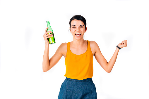 Closeup of a young excited woman having fun while holding a bottle of beer - isolated on white.