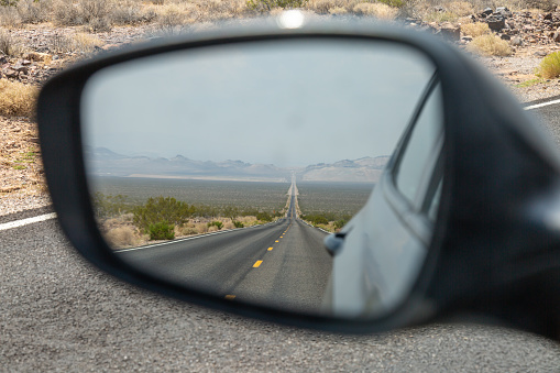 Looking into the rear view mirror of a car, at a long, straight road in Death Valley, California