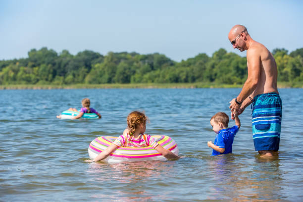 família brincando na água na praia num dia de verão - inner tube swimming lake water - fotografias e filmes do acervo