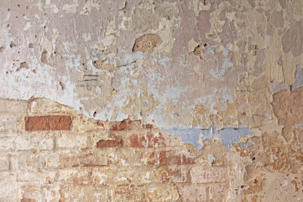 istock Old flaky white paint peeling off a grungy cracked wall. Cracks, scrapes, peeling old paint and plaster on background of old cement wall. An old cement stone wall as vintage cracked. Brick wall. 1023738146