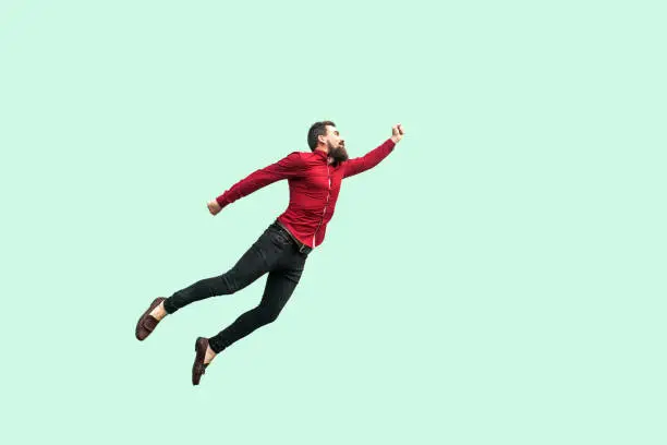 Superman style. Enthusiasm concept. strong bearded businessman felt himself a superhero and flying up. indoor studio shot isolated on light green background.
