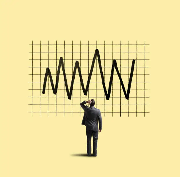 A businessman places his hand on his head as he looks up at a financial chart that shows the volatility of the financial markets.