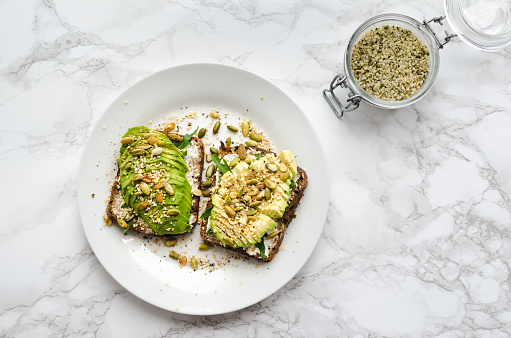 Healthy avocado toasts for breakfast or lunch with rye bread, sliced avocado, arugula, pumpkin, hemp and sesame seeds, salt and pepper. Plant-based diet. Clean eating. Top view. Copy space.