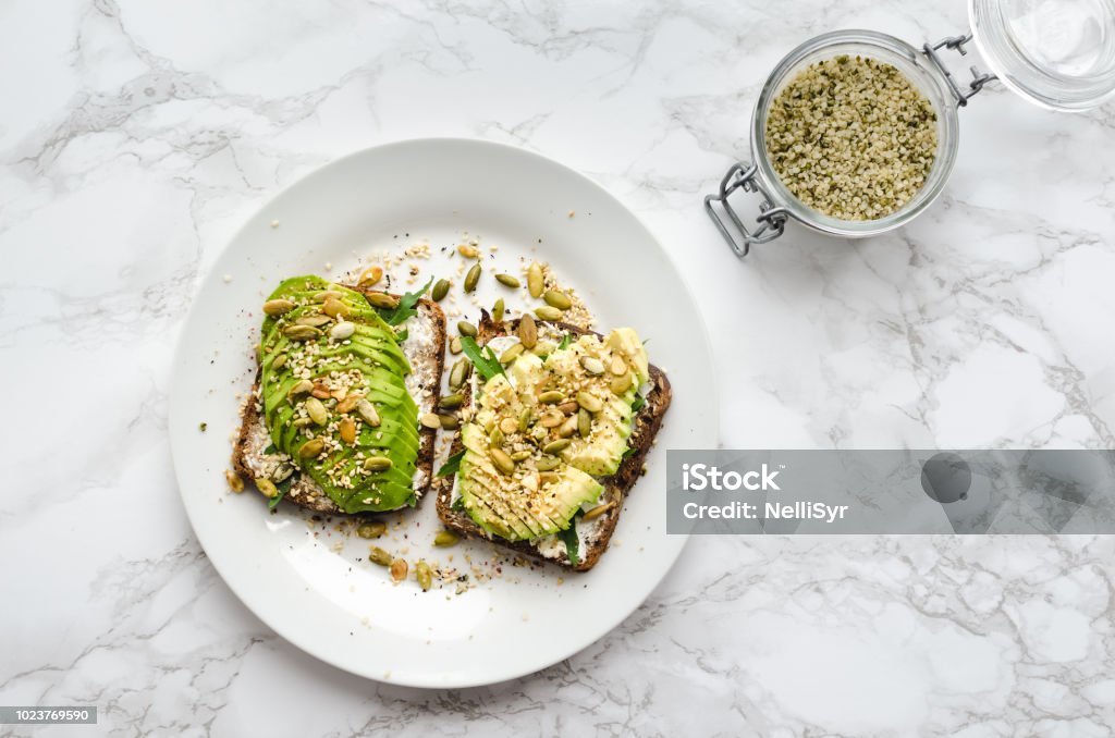 Healthy avocado toasts Healthy avocado toasts for breakfast or lunch with rye bread, sliced avocado, arugula, pumpkin, hemp and sesame seeds, salt and pepper. Plant-based diet. Clean eating. Top view. Copy space. Avocado Stock Photo