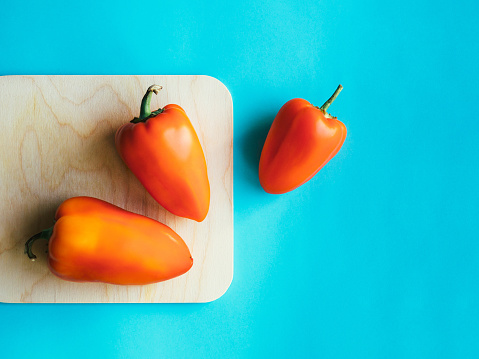 Three big sweet red peppers are lying on cutting board on a blue background