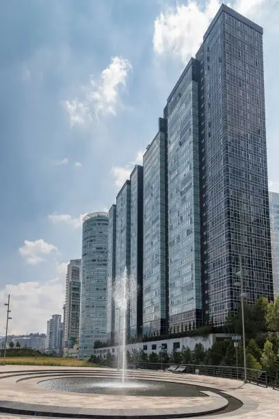 Photo of high modern skyscrapers behind a fountain, beside La Mexicana urban park in Santa Fe, Mexico City