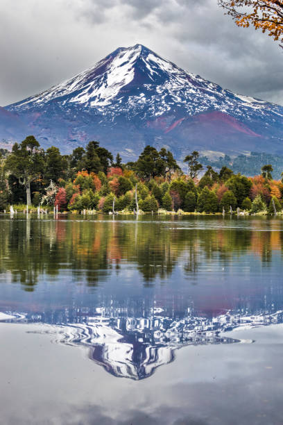 laguna di captren e vulcano llaima durante la stagione autunnale, uno specchio colorato all'interno del parco nazionale di conguillio, cile - volcano lake blue sky autumn foto e immagini stock