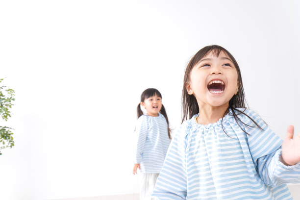Two happy little girls are playing and laughing inside a home environment. Surrounded by toys and a colorful tent, they enjoy a joyful and energetic moment together. The scene captures carefree childhood, friendship, and fun indoor activities