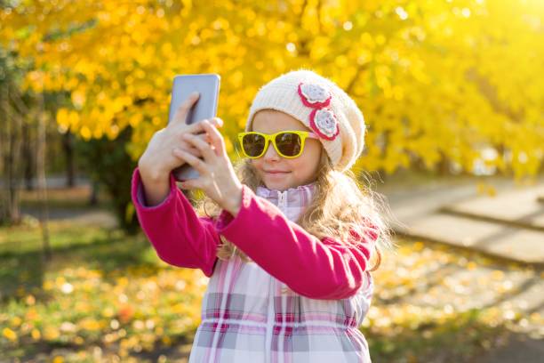 muchacha bonita de 7 años haciendo selfie utilizando un smartphone, otoño de fondo. - 6 7 years lifestyles nature horizontal fotografías e imágenes de stock