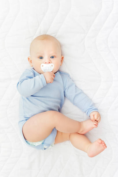 Chico lindo bebé con chupete en mono azul acostado en cama - foto de stock