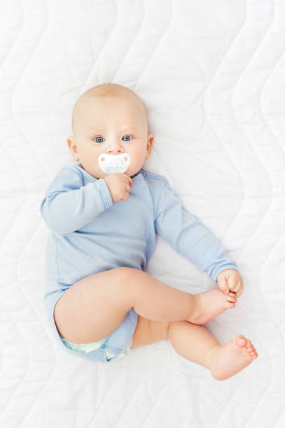 istock Cute baby boy with pacifier in blue onesie lying on bed 1023923358