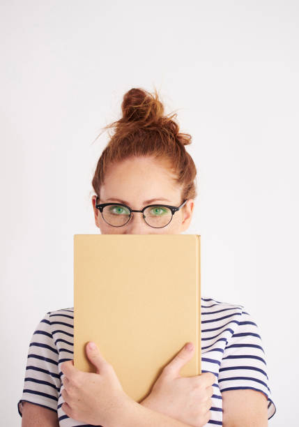 ritratto di studente in possesso di un libro in studio girato - vertical caucasian glasses red hair foto e immagini stock