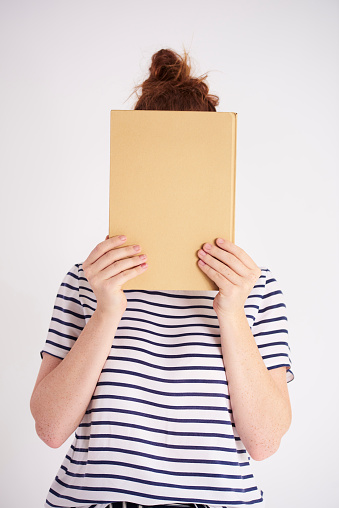Young woman covering her face with book at studio shot