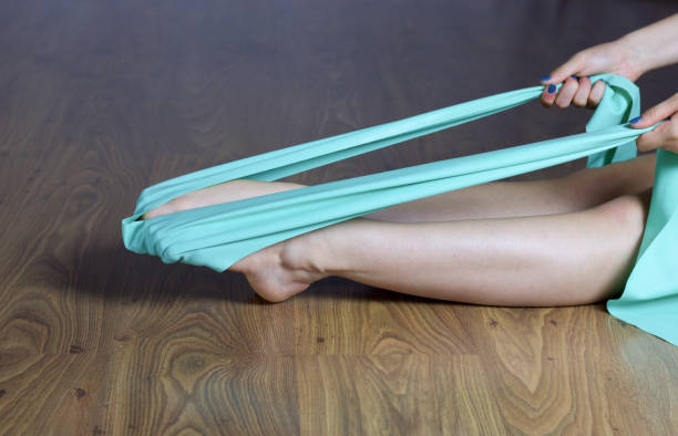 mujer piernas haciendo ejercicios para pies segó con banda elástica, sentado en el piso de madera - exercices fotografías e imágenes de stock