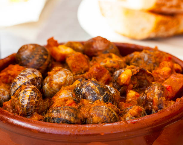 クローズ アップ - ��伝統的なスペインのタパスのニンニクと黒鉄フライパンで唐辛子トマトソース トマト煮のカタツムリ - gourmet snail food escargot ストックフォトと画像